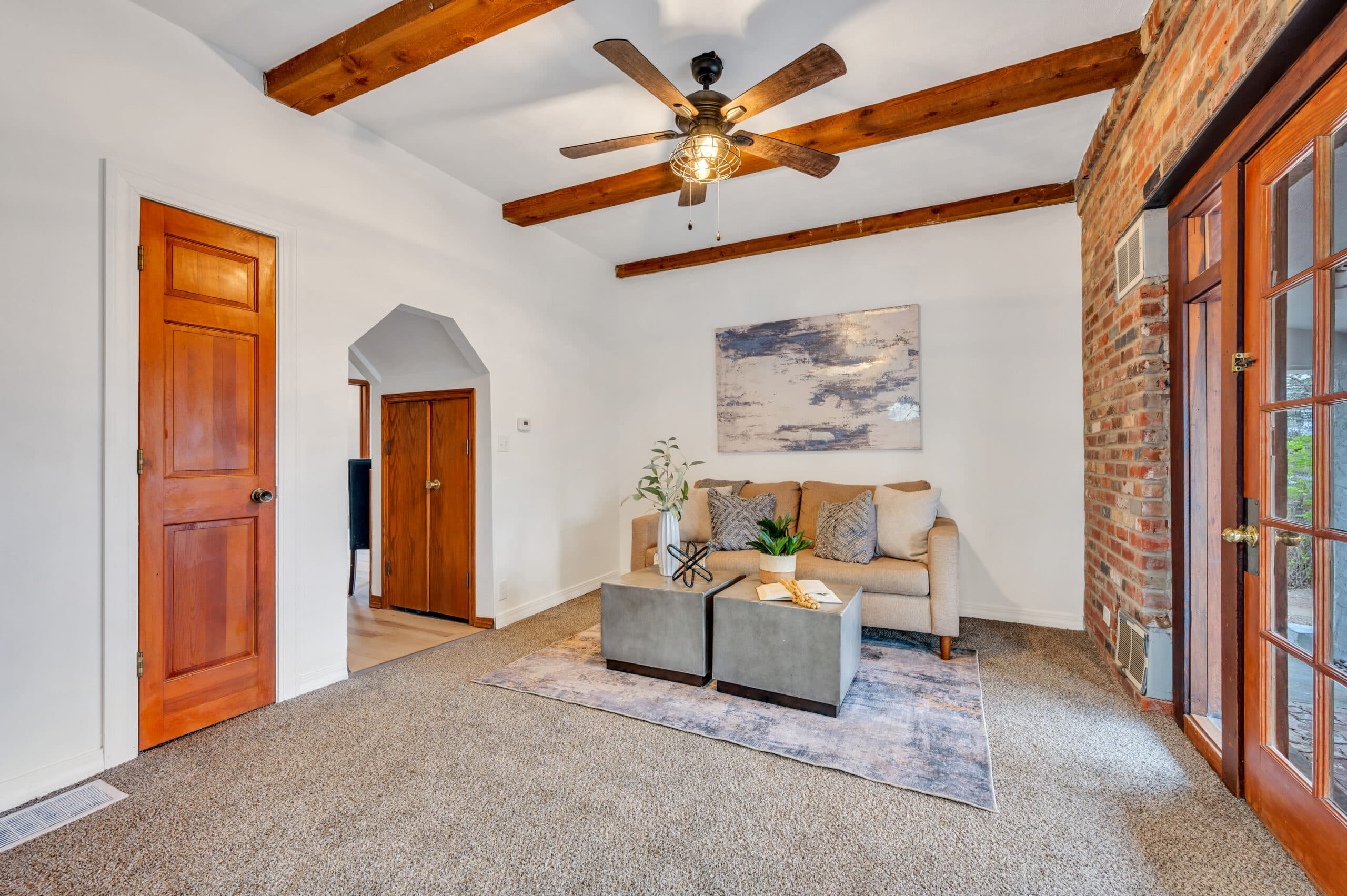 Living room with exposed wooden ceiling beams, brick accent wall, and cozy neutral decor.