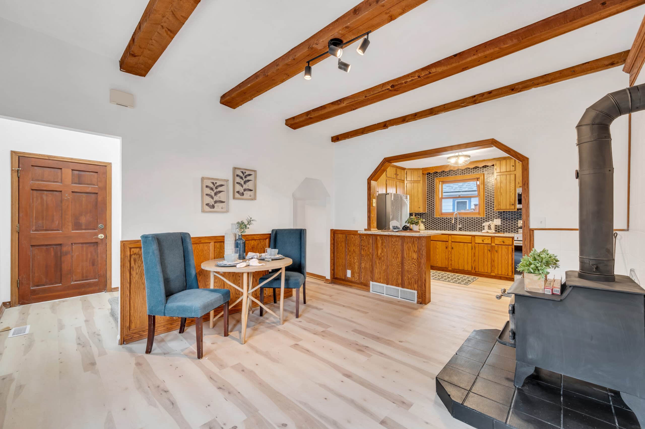 Dining area with exposed wood beams, modern light fixtures, and open kitchen with wood cabinetry.