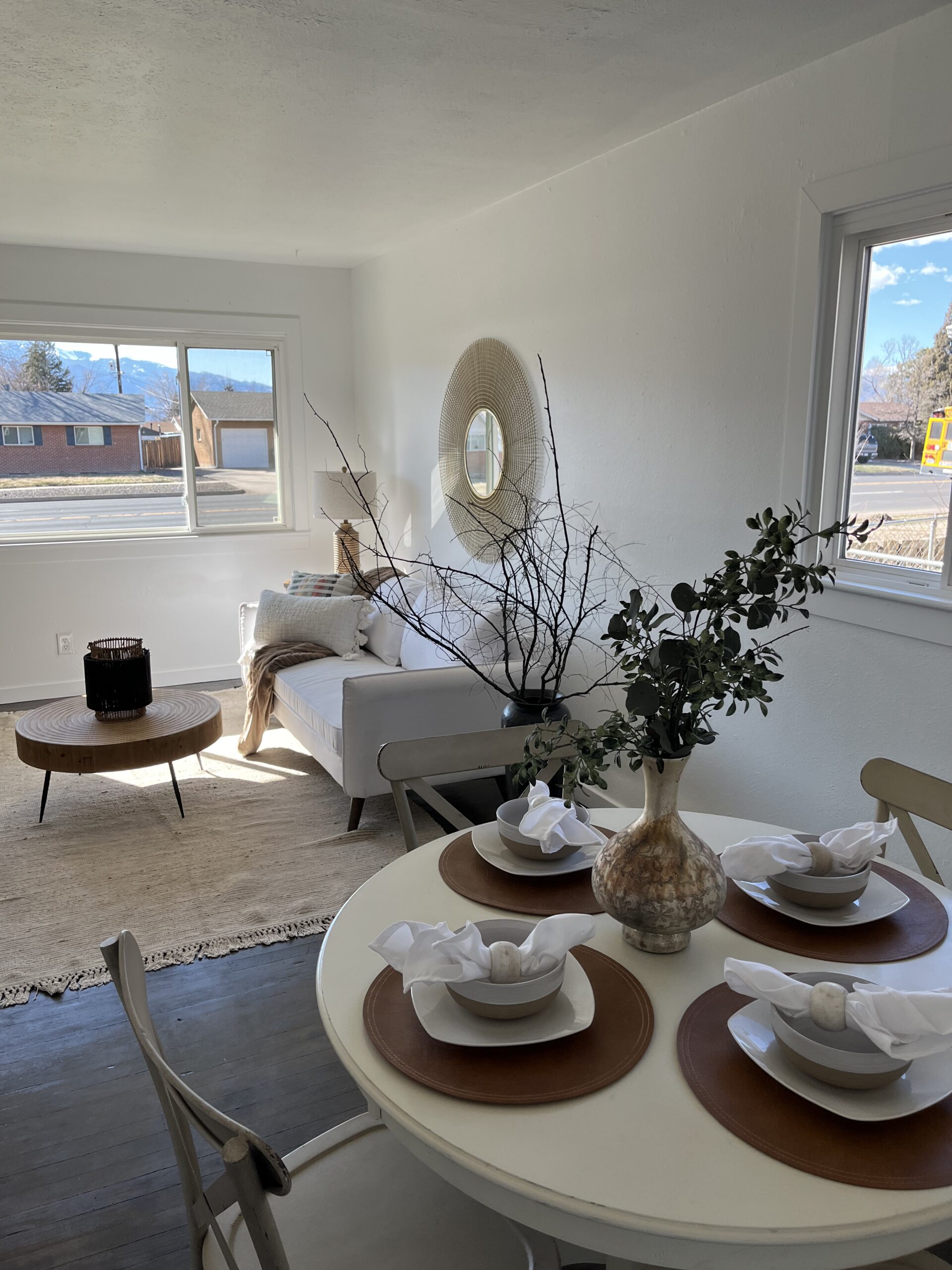 Open living and dining area with white walls, modern furniture, and natural light from large windows.