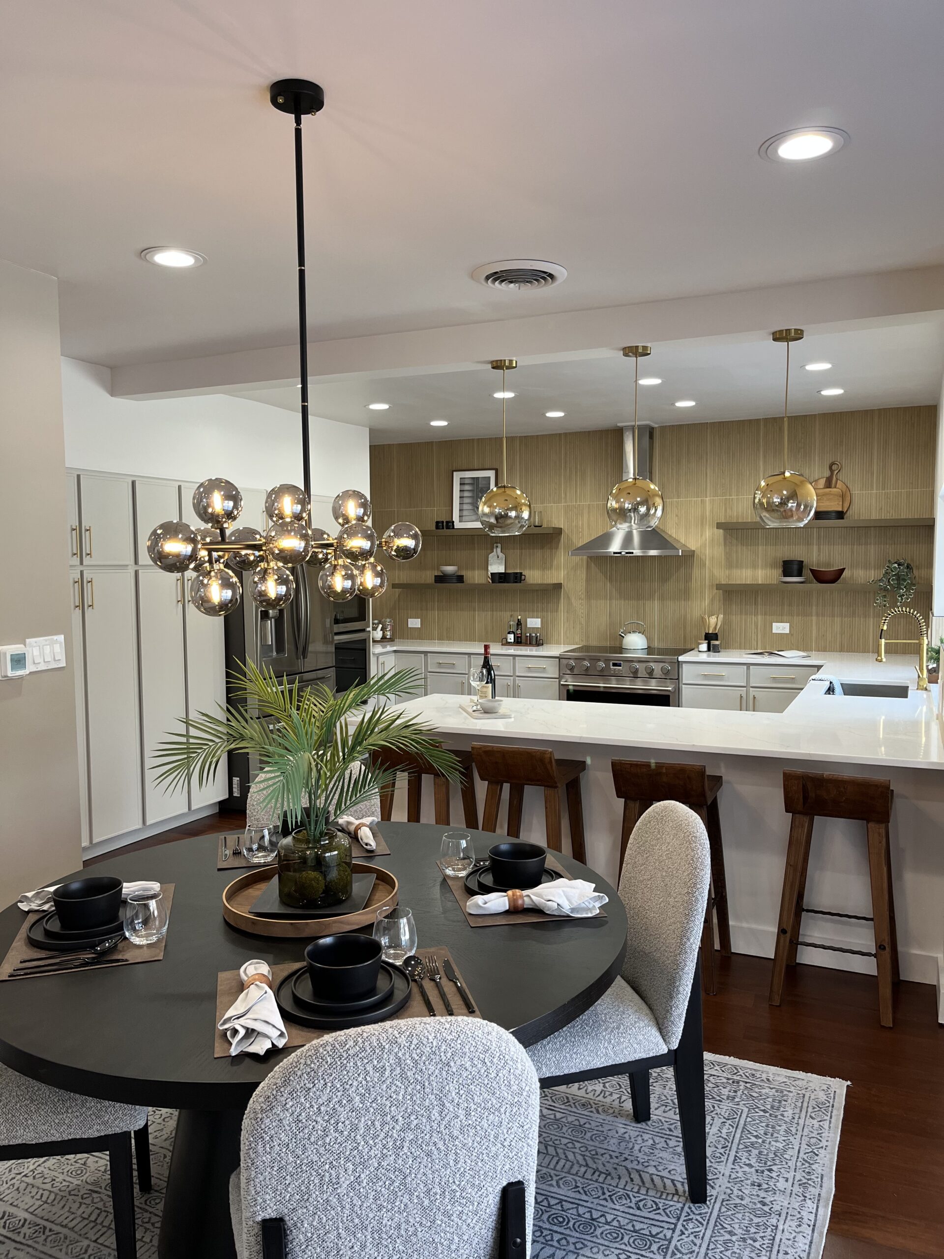 Contemporary kitchen with open dining area, wood accents, white cabinetry, and gold lighting fixtures.