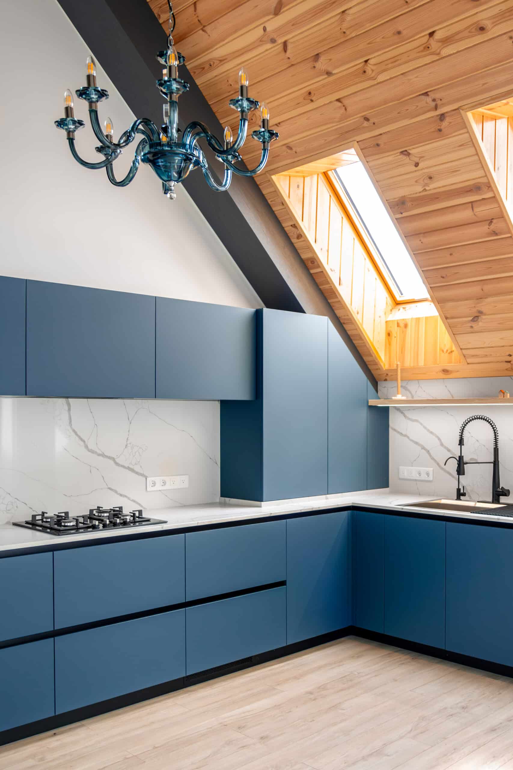 Modern attic kitchen with custom blue cabinets, marble backsplash, and wood-paneled ceiling.