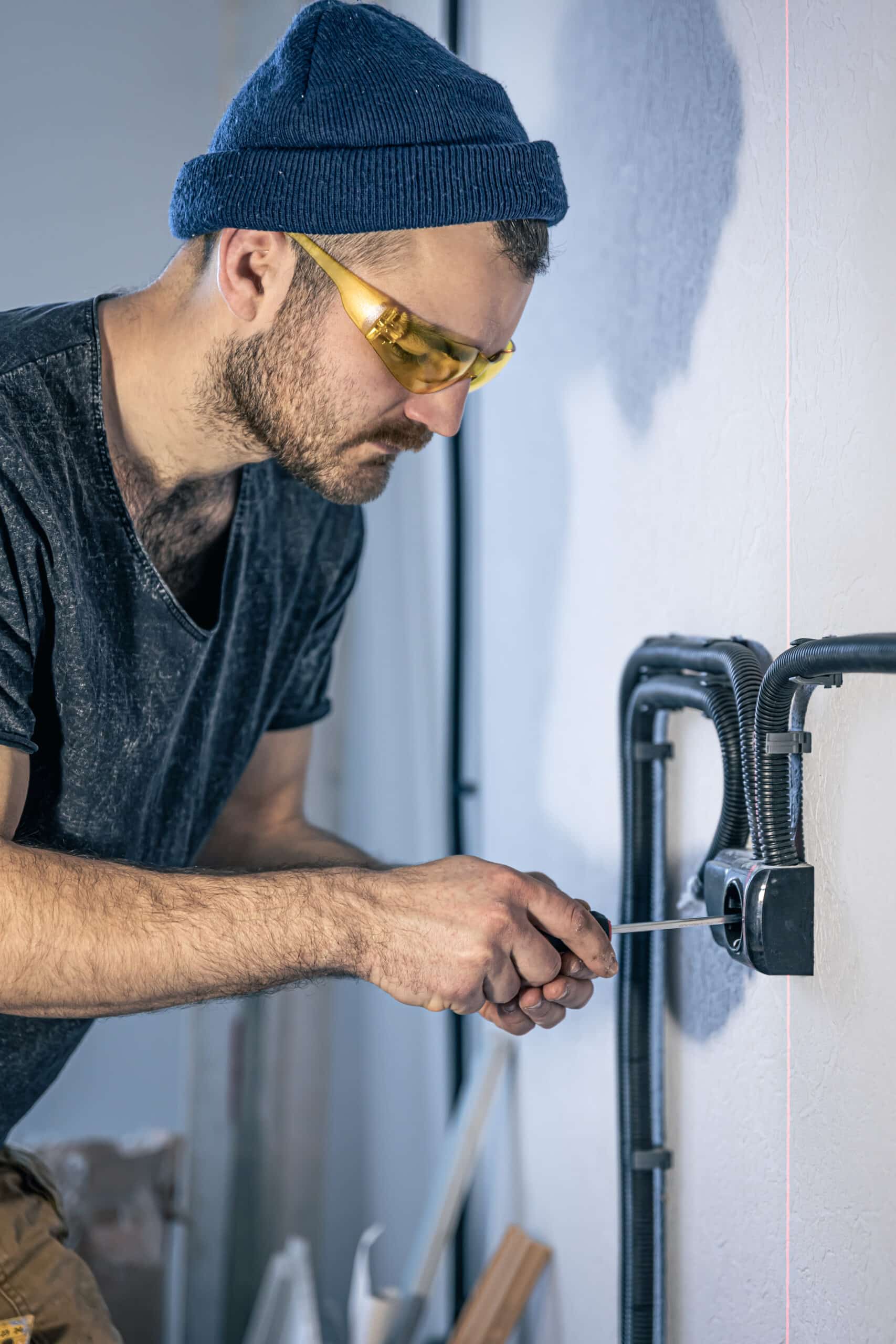 Handyman using a screwdriver to repair electrical wiring on a wall.