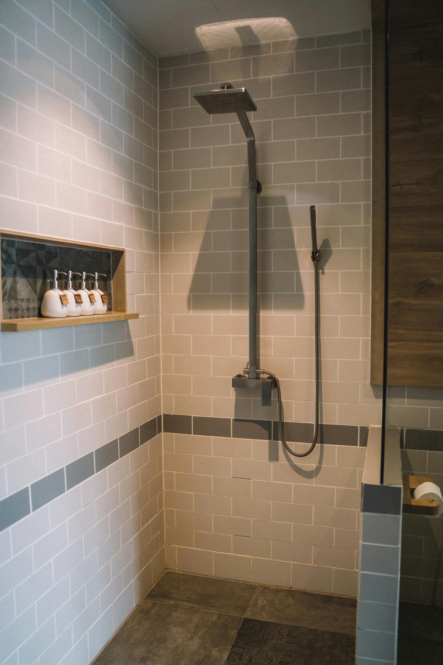 Modern walk-in shower with light gray subway tile walls, dark accent strip, and built-in niche shelf.