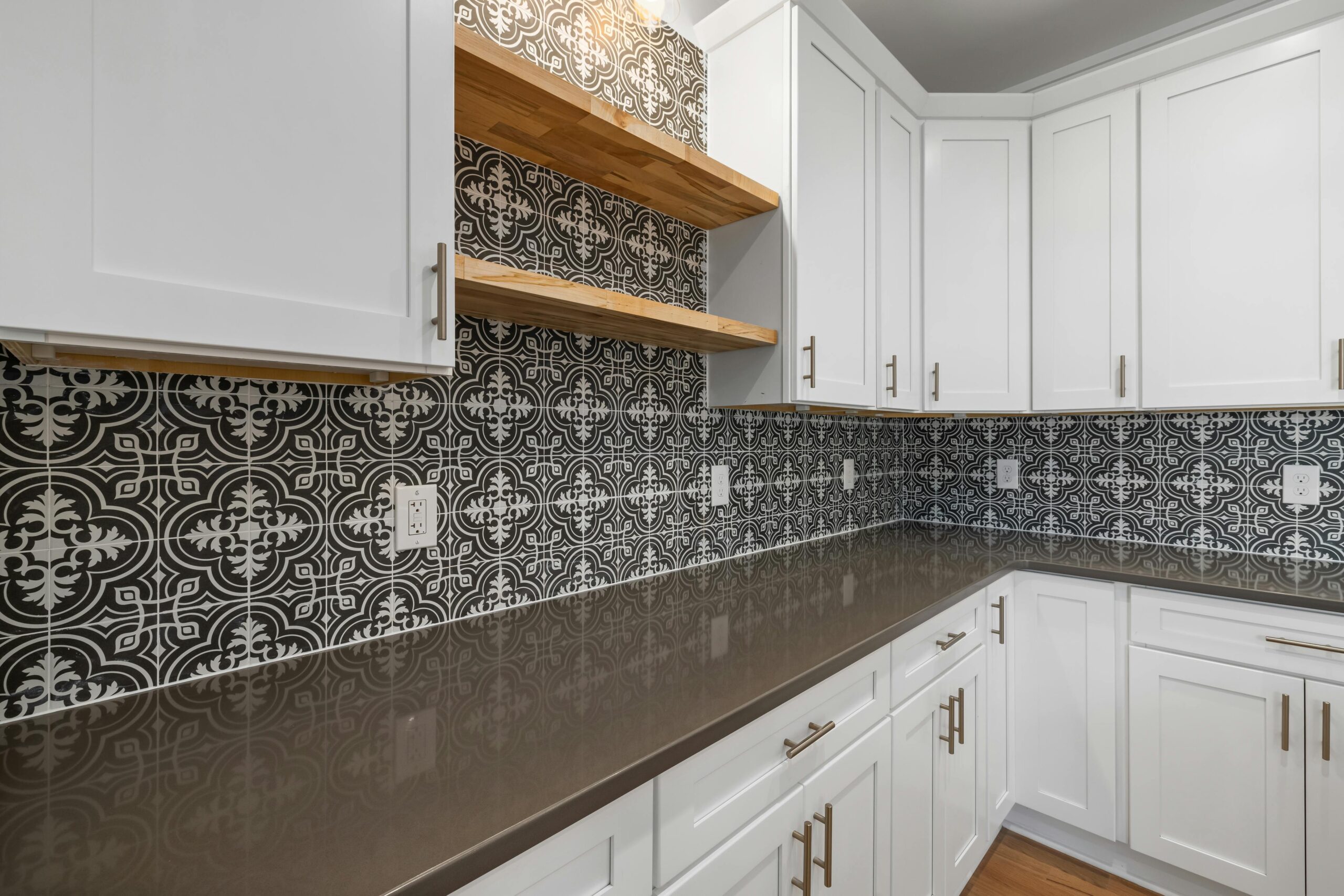 Kitchen backsplash with patterned black and white tile, white cabinets, and wooden shelves.