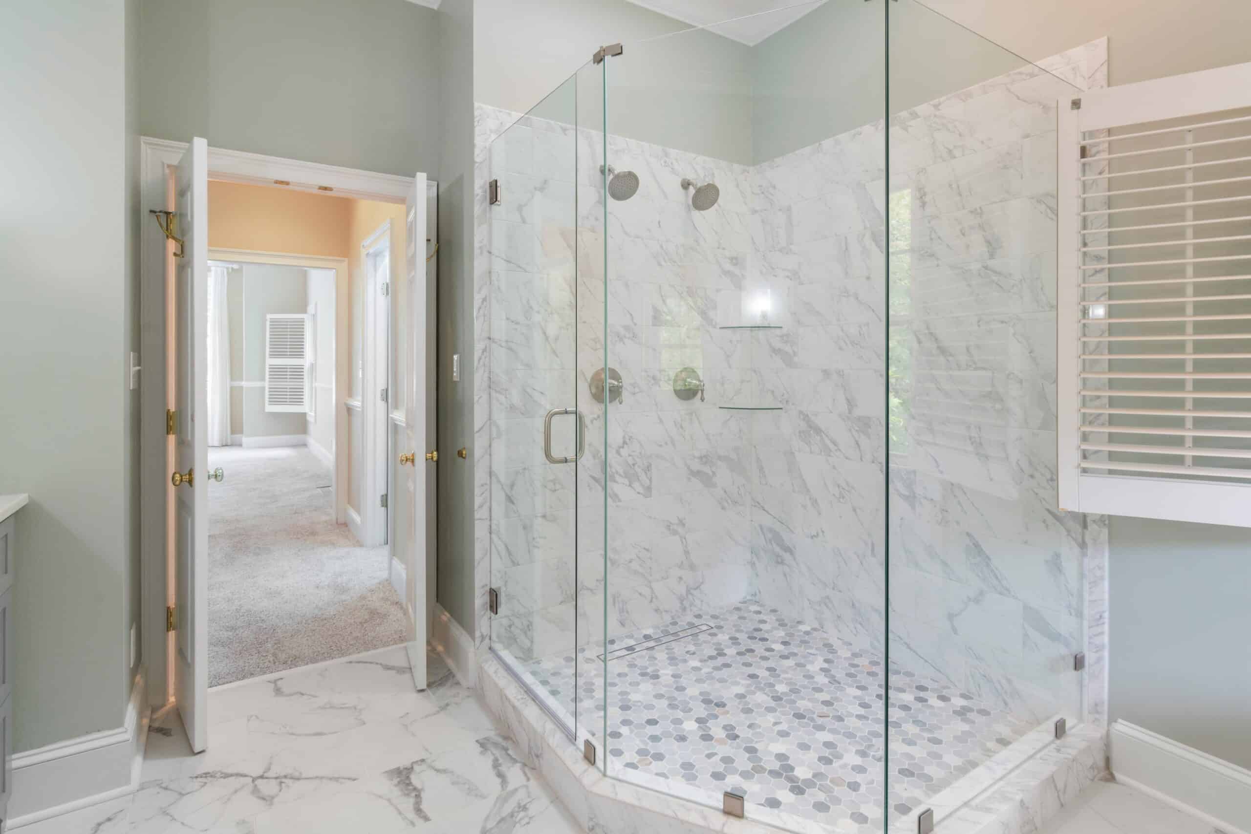Luxury bathroom featuring a custom marble tile shower with glass doors and hexagon floor tile.